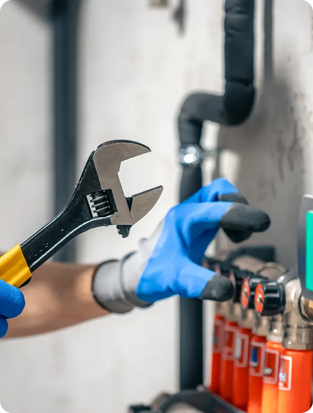 Person wearing gloves adjusting a pipe valve with a wrench